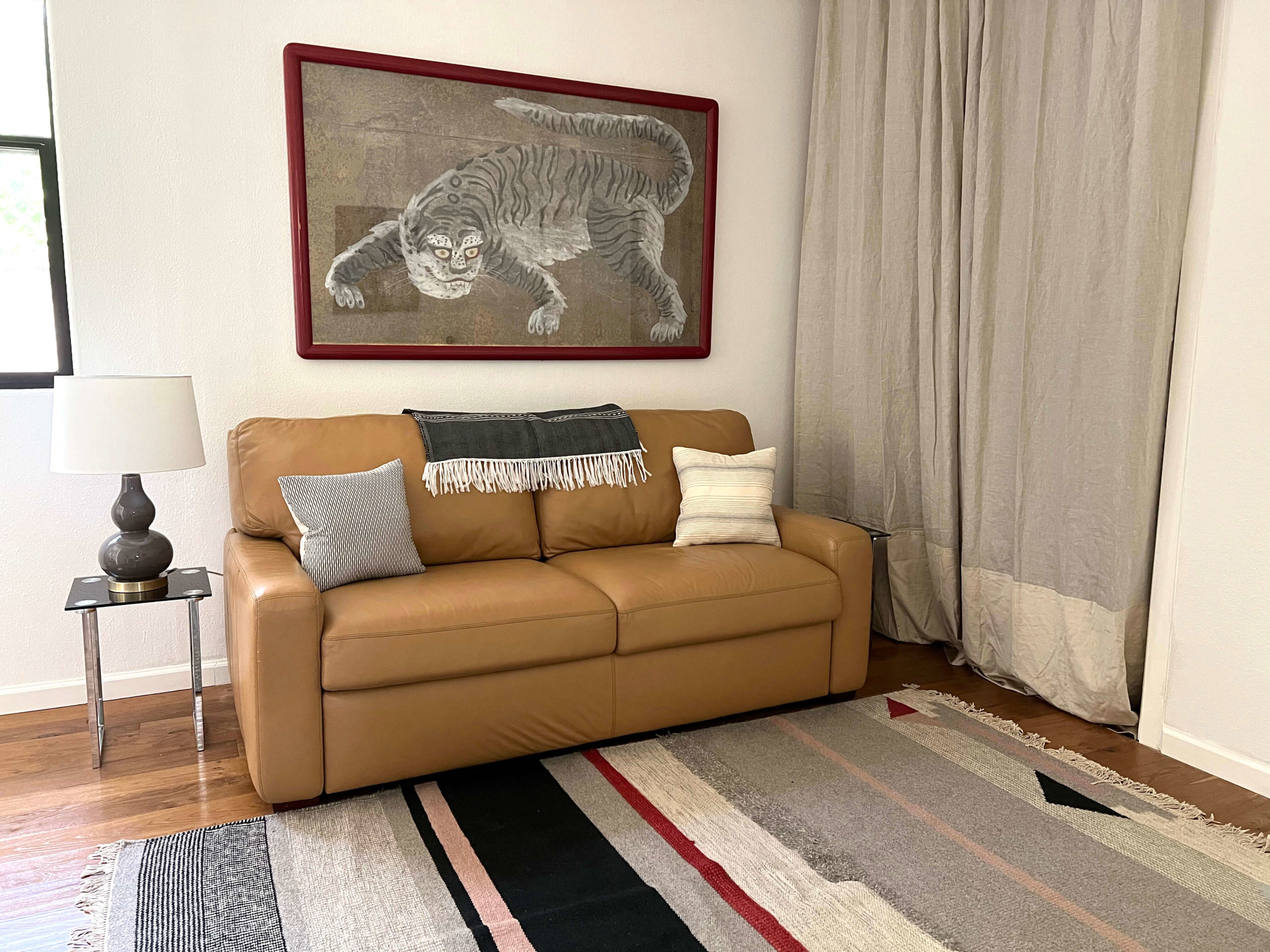 Fold-out leather couch in living/bedroom of Bouldin Creek Airbnb in South Austin, Texas, tiger red framed art hanging, red and grey striped rug