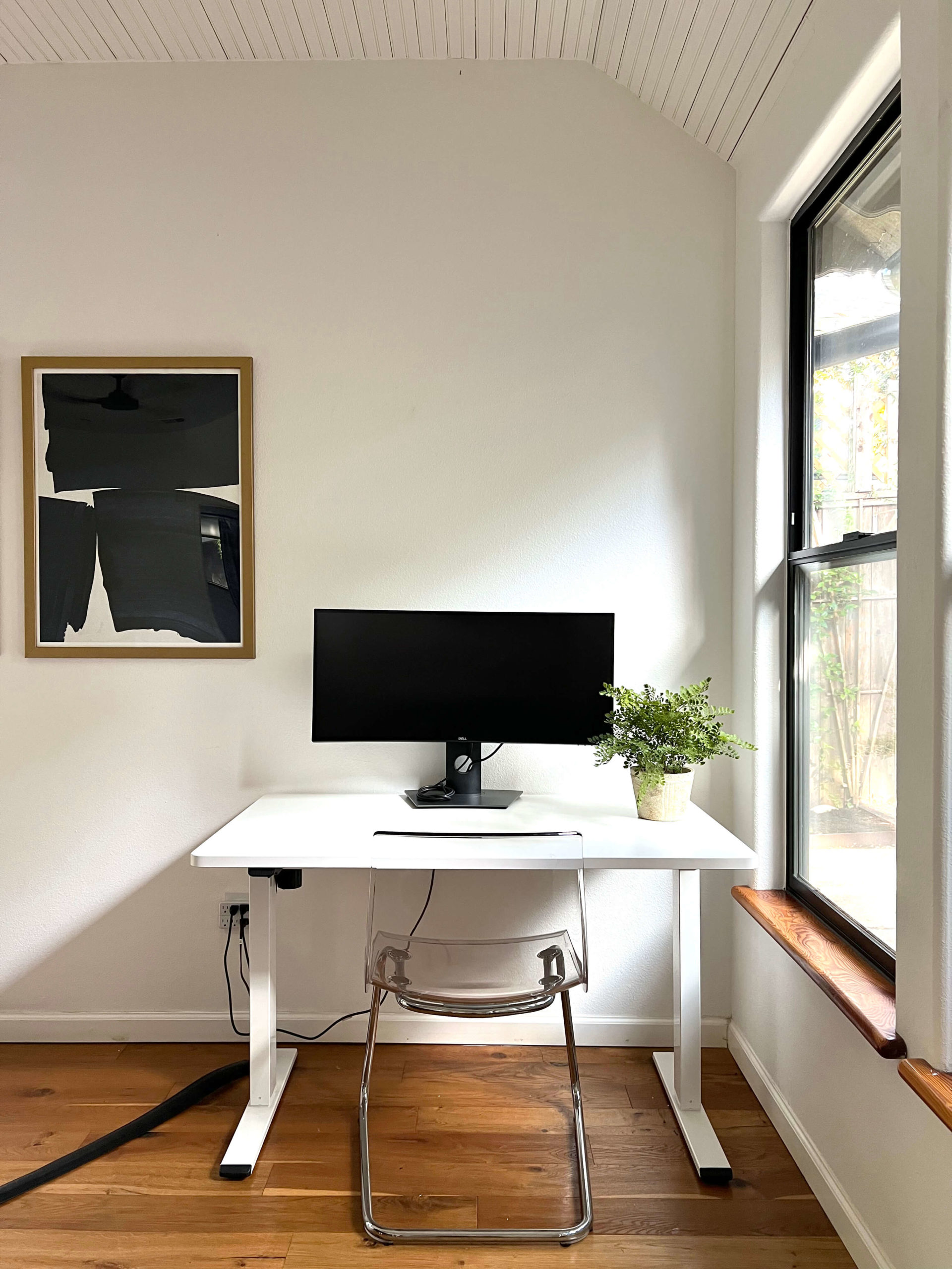 Desk in living room of Bouldin Creek Airbnb in South Austin, Texas, computer monitor, white desk, clear chair, black and white abstract painting on wall