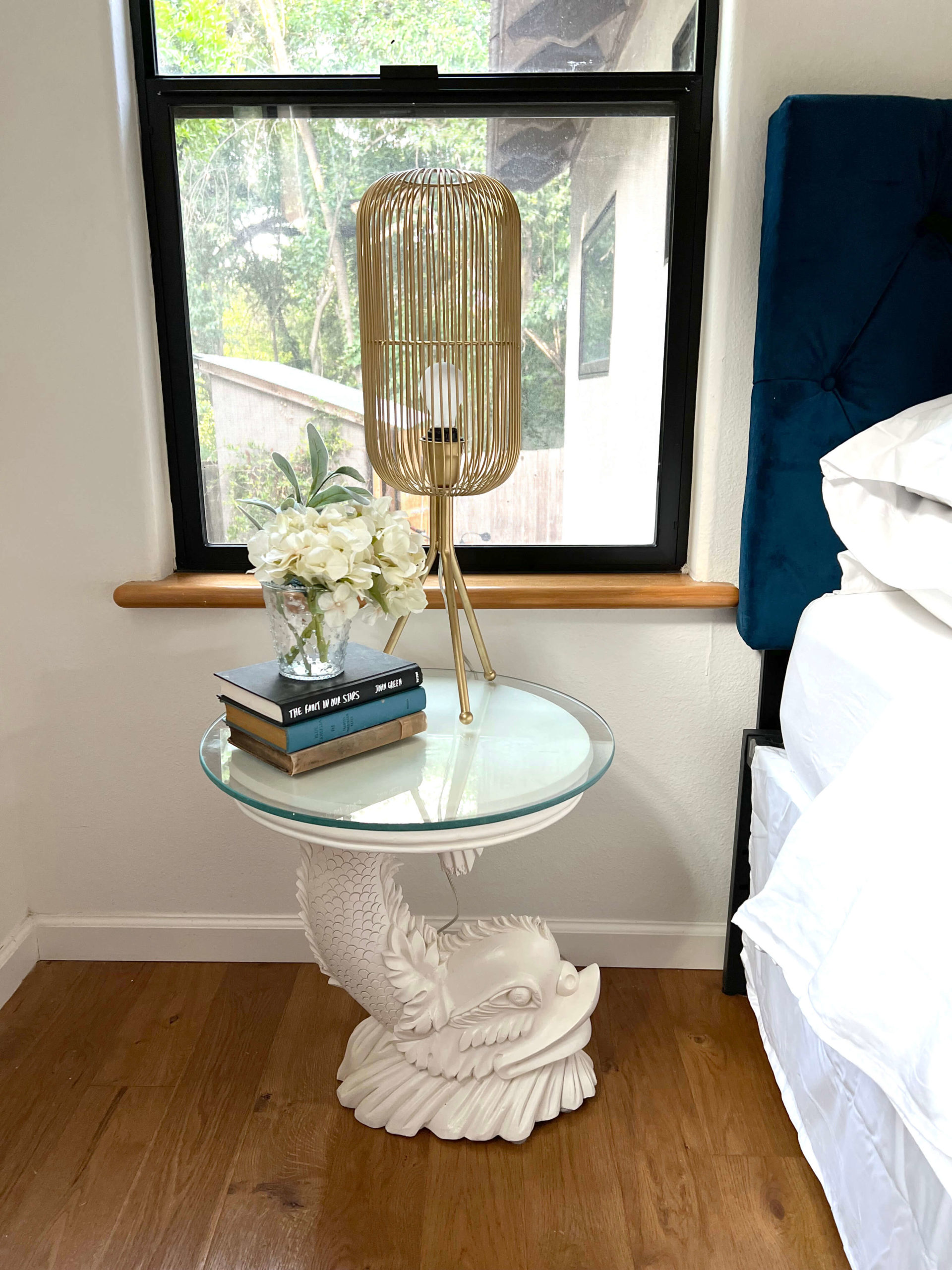 White fish-shaped nightstand in bedroom of Bouldin Creek Airbnb in South Austin, Texas, gold lamp and stack of books