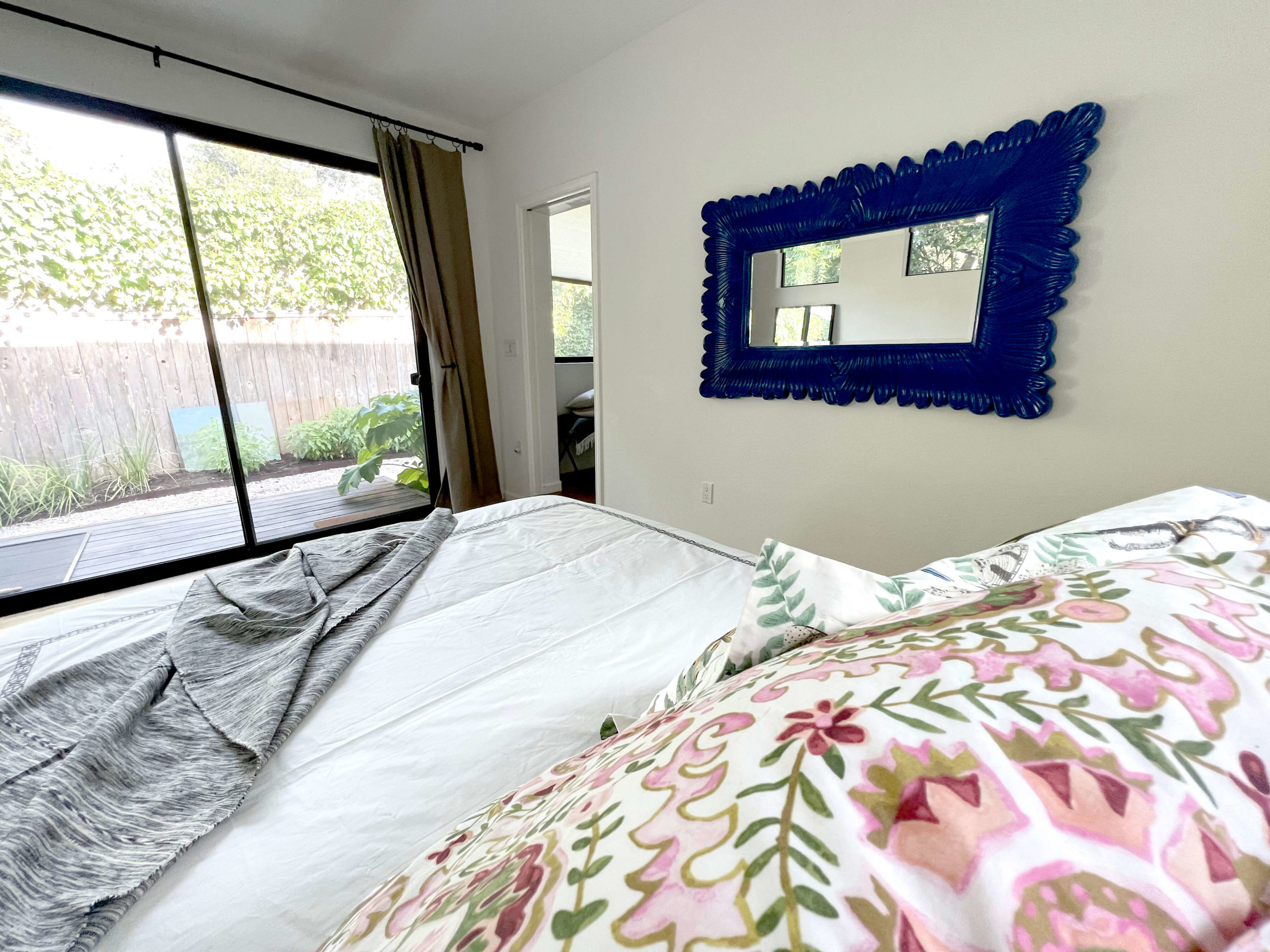 Blue horizontal mirror in main bedroom of Bouldin Creek Airbnb in South Austin, Texas, floral pillow, sliding door out to patio