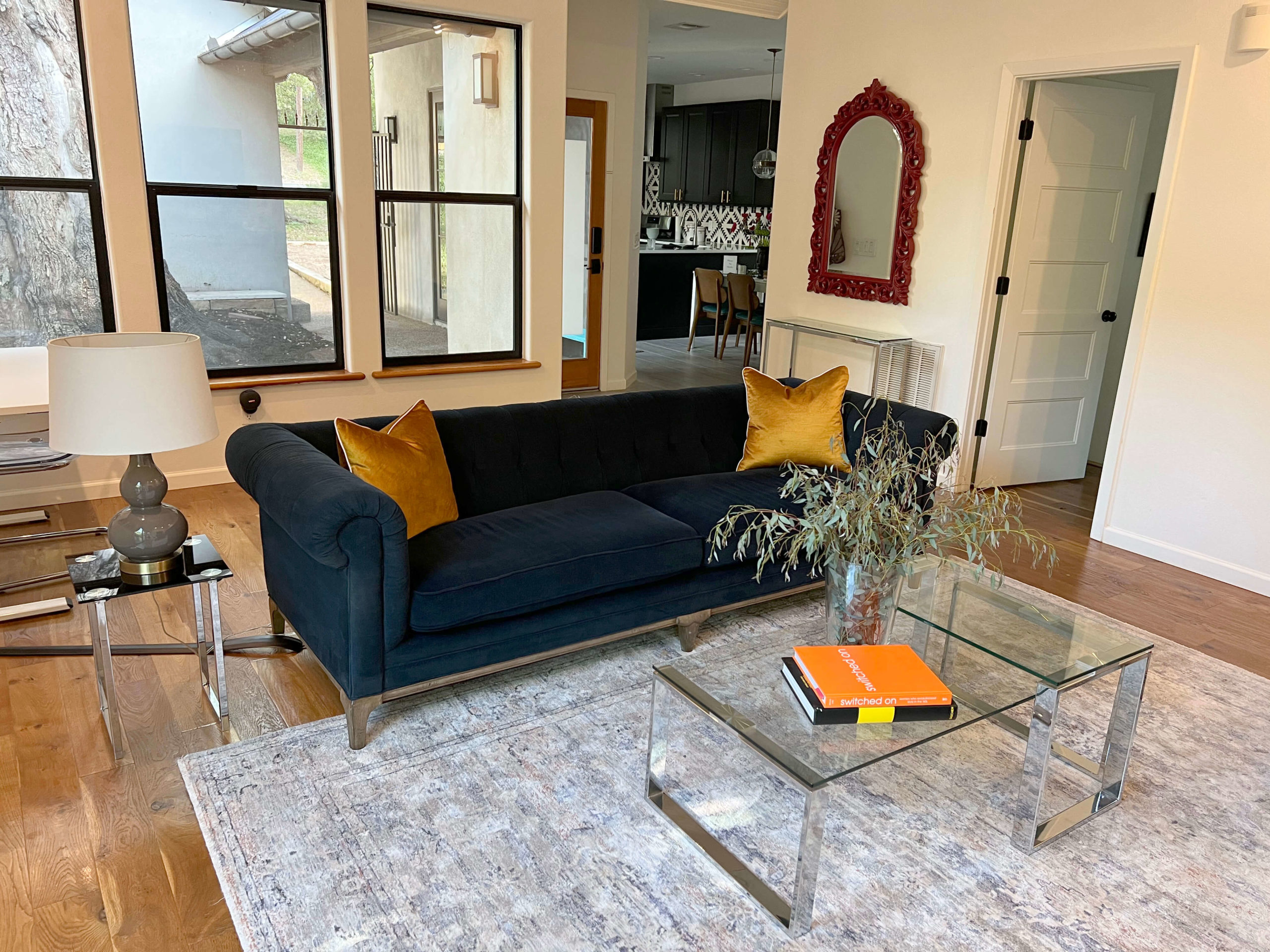 Living room of Bouldin Creek Airbnb in South Austin, Texas, blue velvet couch, yellow pillow, red mirror, clear coffee table